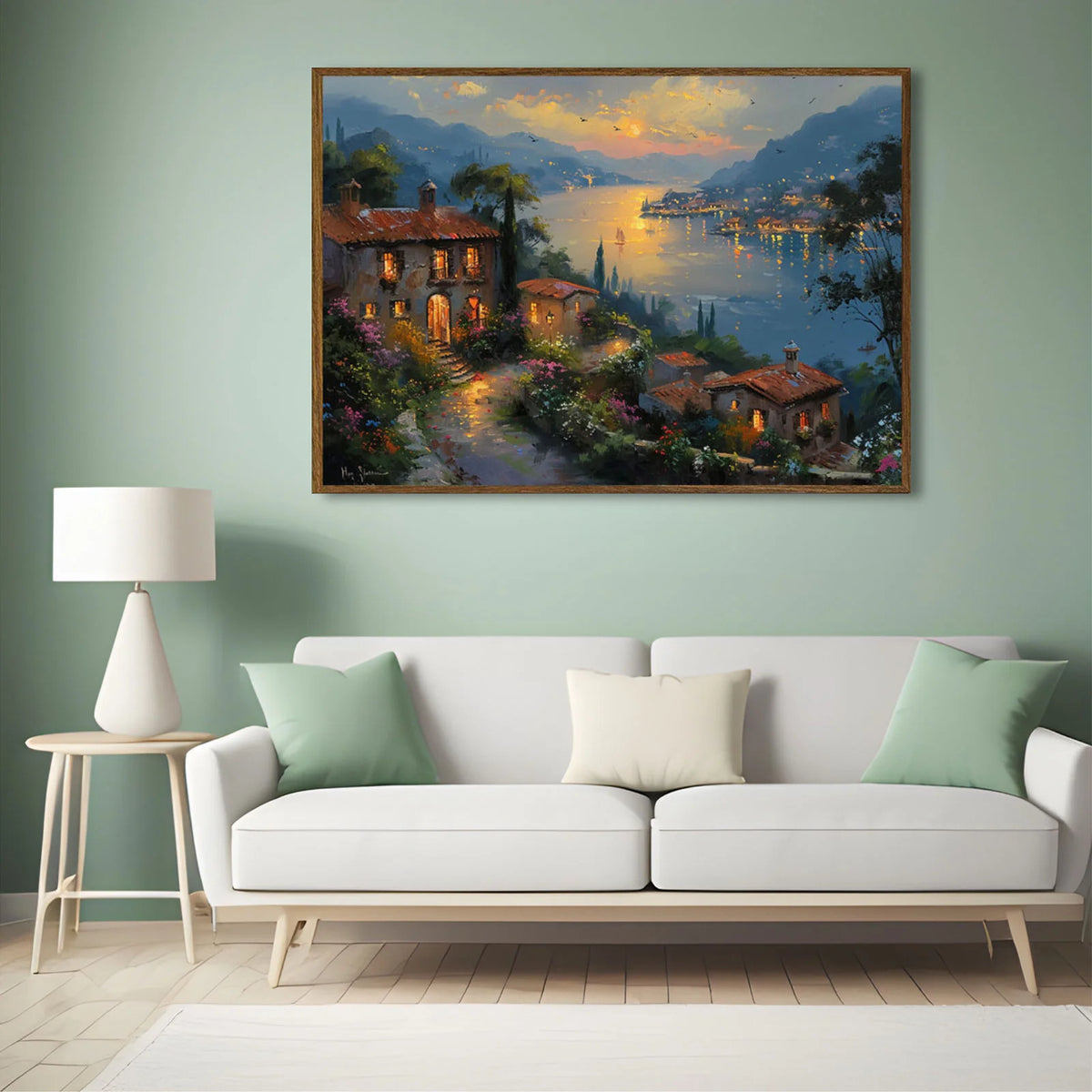 Framed Mediterranean landscape painting hung above a living room sofa displaying warm evening light and coastal villa rustic decor style.